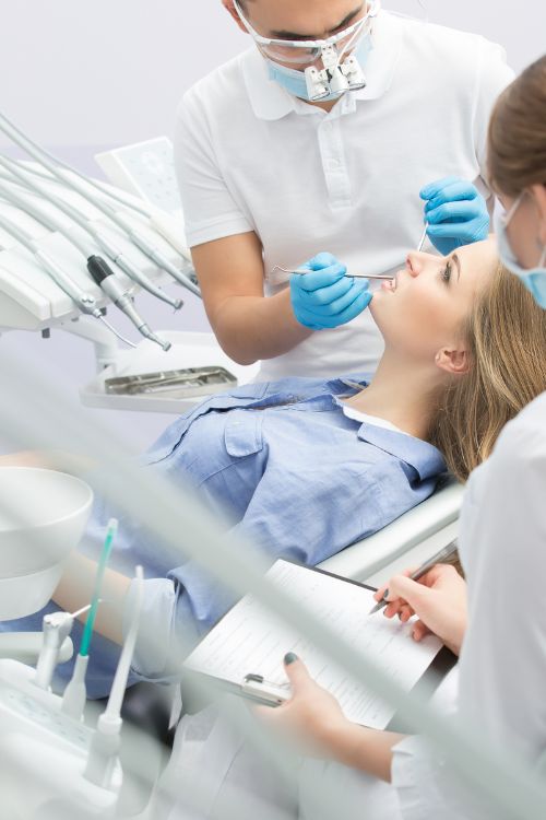 Kobieta leży na fotelu dentystycznym i ma wykonywany zabieg przez dentystę